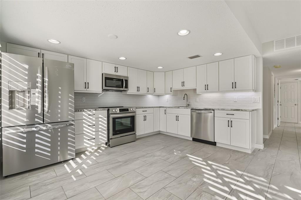 A modern kitchen features white cabinets, stainless steel appliances, and light gray tiled flooring — 5055 N BEACH ROAD UNIT 108, ENGLEWOOD, FL