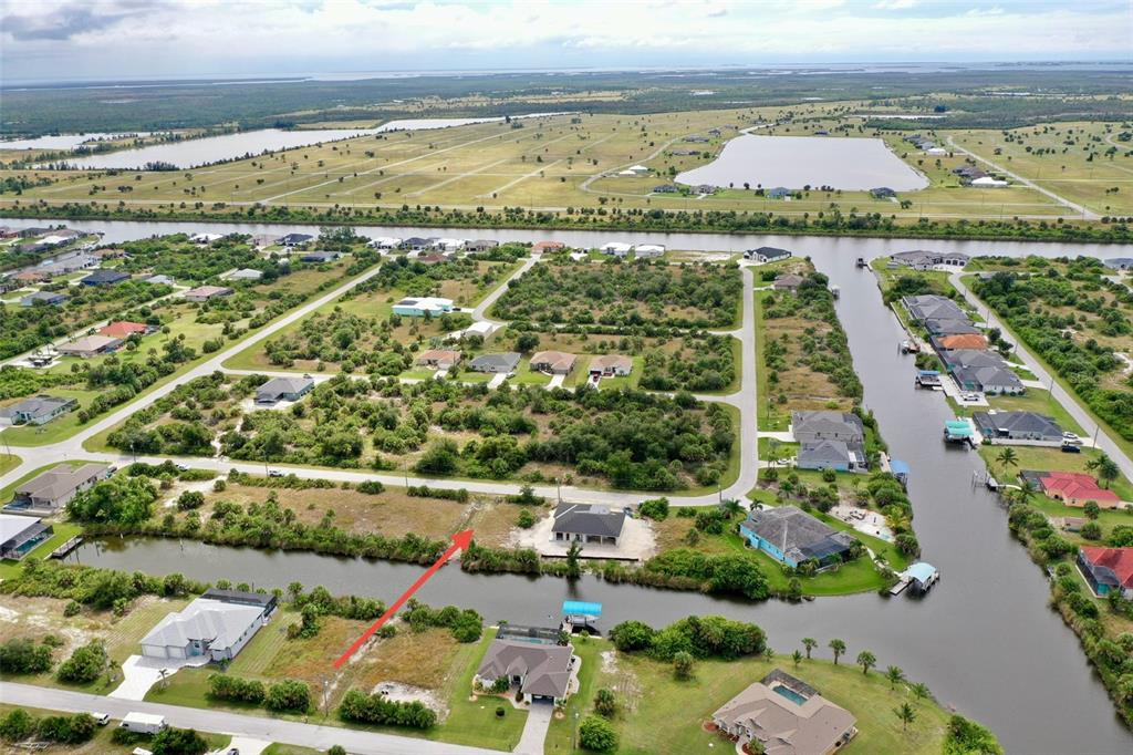 An aerial view shows a vacant waterfront lot with a red arrow pointing toward it — 10868 MCALESTER CIRCLE, PORT CHARLOTTE, FL