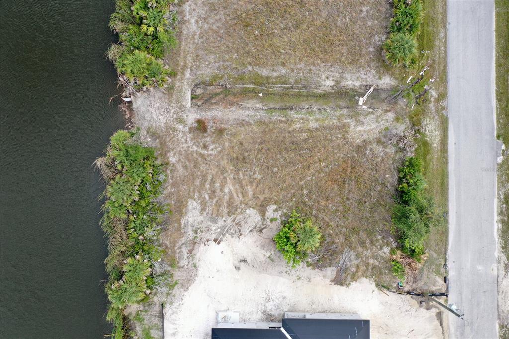 An aerial view shows a vacant waterfront lot next to a road and a house — 10868 MCALESTER CIRCLE, PORT CHARLOTTE, FL