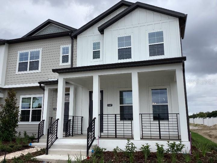 A two-story townhouse exterior features white vertical siding, a covered front porch, and metal railings — 13407 LEMON ORCHARD BEND, WINDERMERE, FL