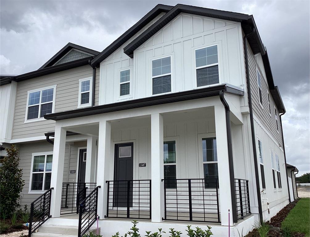 A two-story townhouse exterior features white vertical siding, a covered front porch, and black railings — 13407 LEMON ORCHARD BEND, WINDERMERE, FL