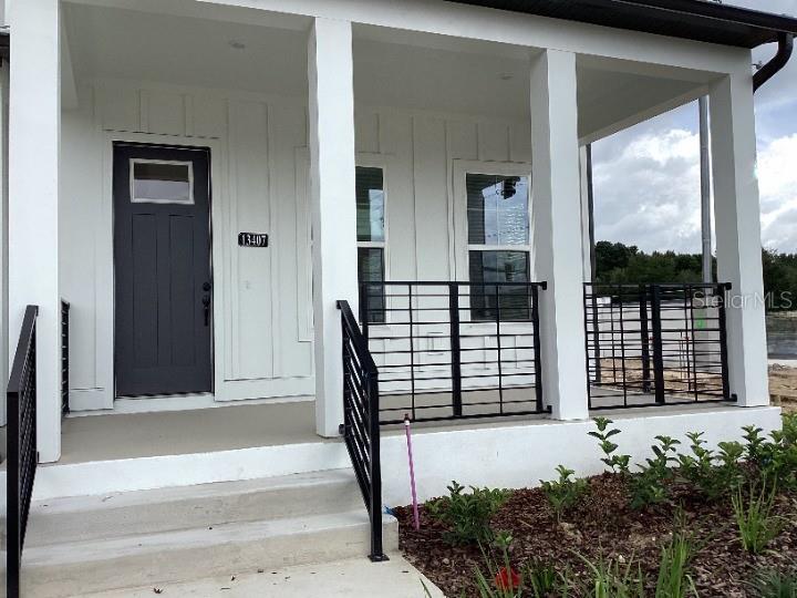 A white house exterior features a dark front door, concrete steps, and black metal railings — 13407 LEMON ORCHARD BEND, WINDERMERE, FL