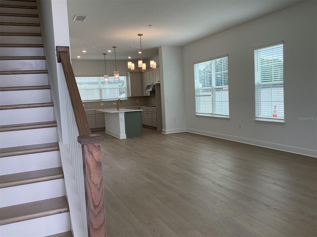 An open-concept kitchen and living area features light wood flooring and a staircase — 13407 LEMON ORCHARD BEND, WINDERMERE, FL