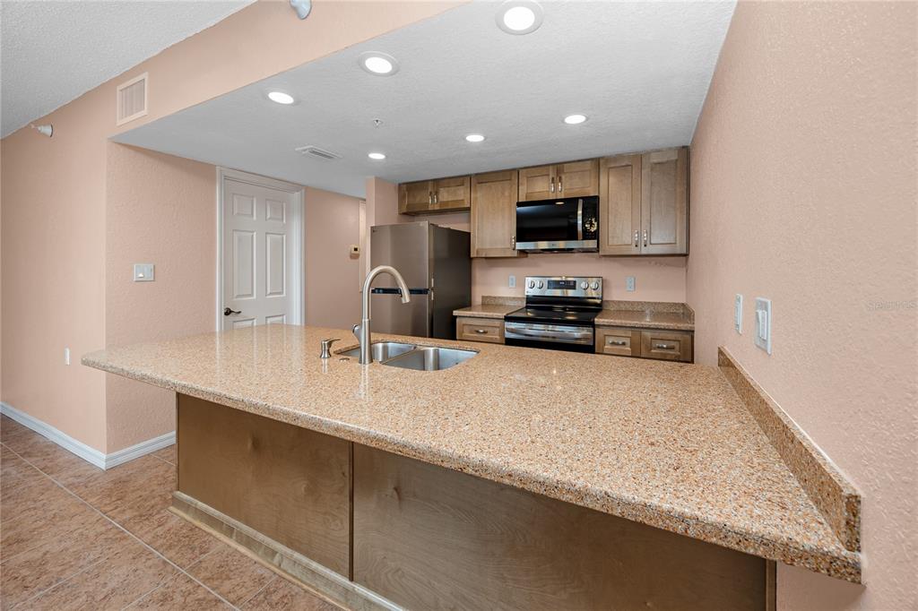 A kitchen features a granite-topped island, stainless steel appliances, and light wood cabinetry — 50 GULF BOULEVARD UNIT 108, INDIAN ROCKS BEACH, FL
