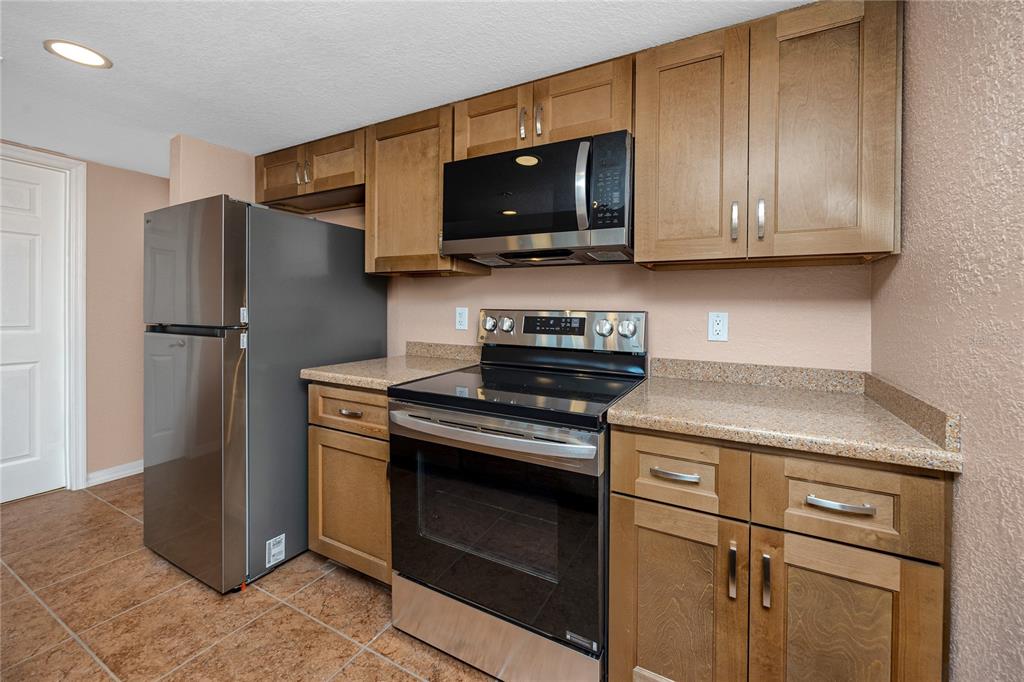 A kitchen features wood cabinets, stainless steel appliances, and tan countertops over tile flooring — 50 GULF BOULEVARD UNIT 108, INDIAN ROCKS BEACH, FL