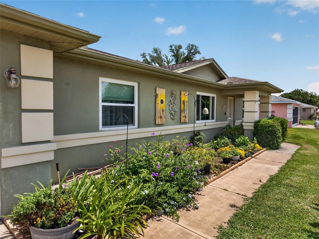 The exterior of a green house features a concrete walkway, garden beds, and decorative wall art — 6341 SW 103RD LANE, OCALA, FL