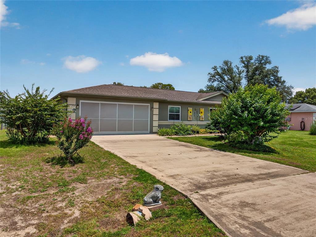 A single-story house with a concrete driveway, a large garage door, and surrounding landscaping — 6341 SW 103RD LANE, OCALA, FL