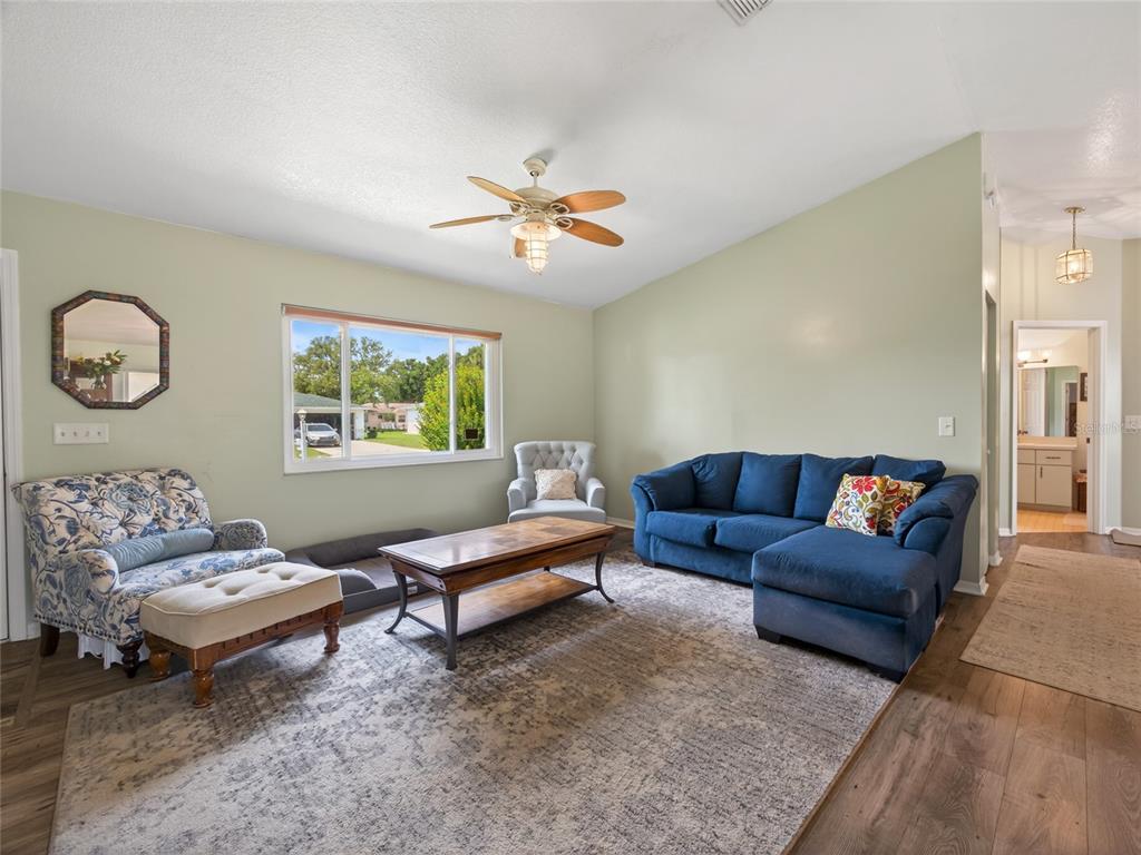 A living room features a blue sectional sofa, patterned armchair, wood coffee table, and rug — 6341 SW 103RD LANE, OCALA, FL