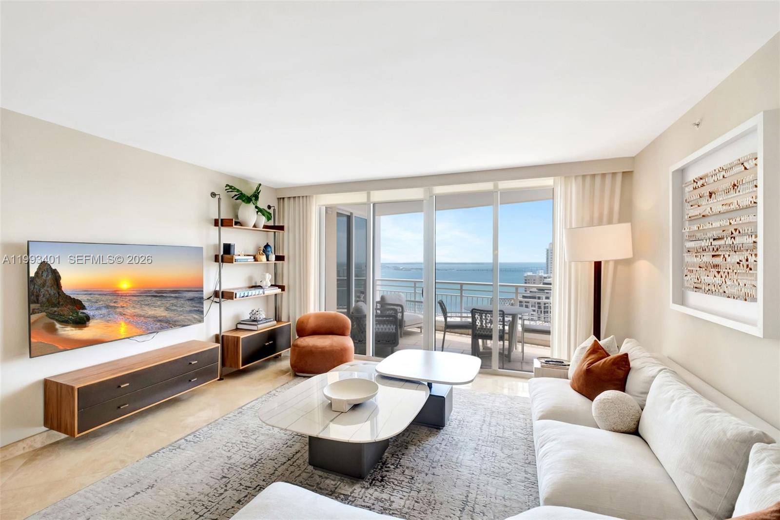 A modern living room features a white sofa, marble coffee tables, and a balcony overlooking water — 848 Brickell Key Dr # 2605, Miami FL 33131, MIAMI, FL