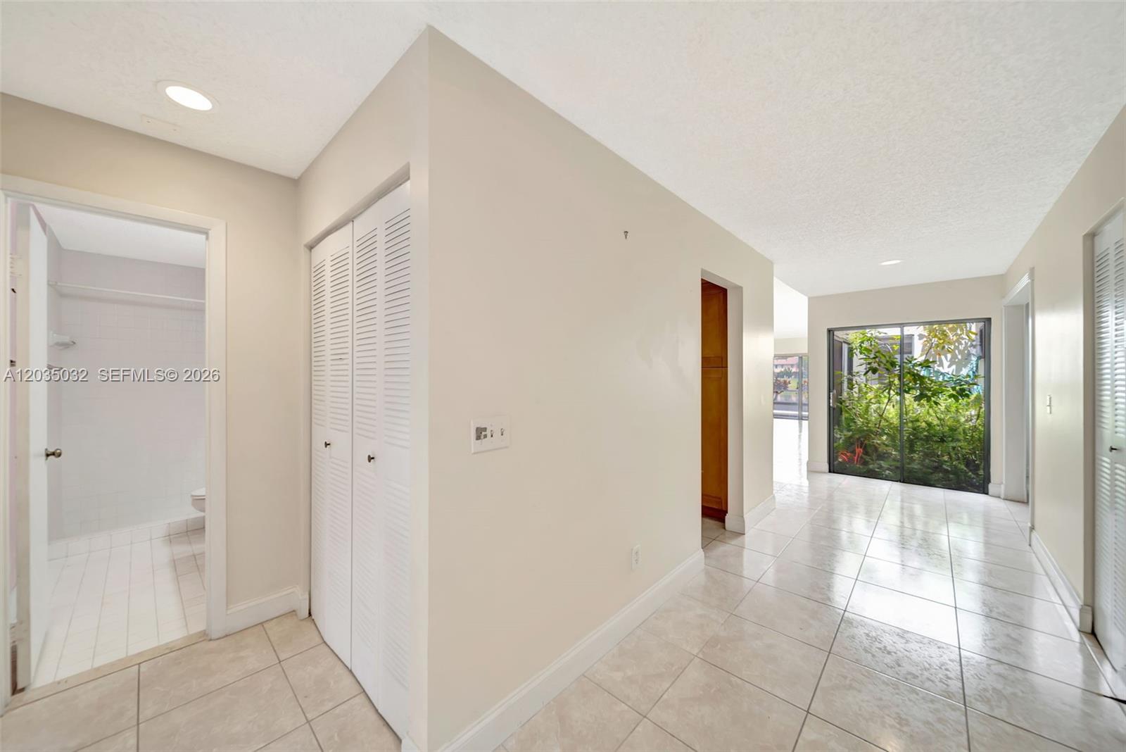A hallway with tiled floors leads to a sliding glass door overlooking lush green foliage — 5223 W Gate Lake Rd # 5223, Tamarac FL 33319, TAMARAC, FL