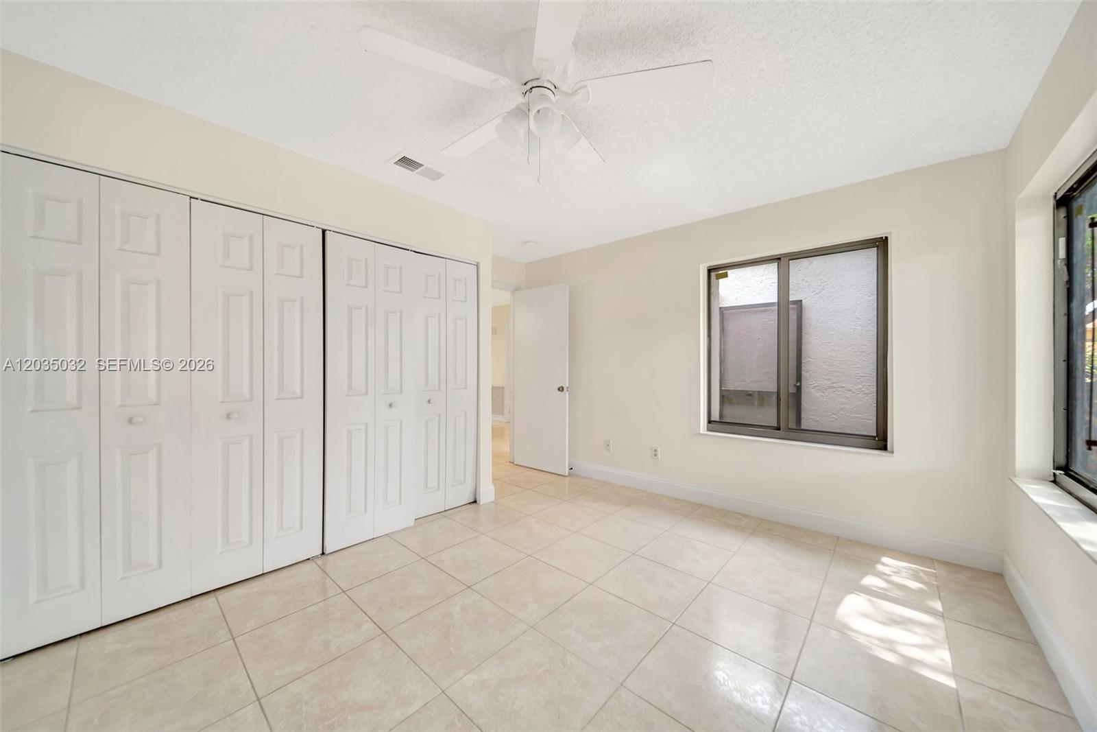 An empty bedroom features white walls, tile flooring, a ceiling fan, and large closet doors — 5223 W Gate Lake Rd # 5223, Tamarac FL 33319, TAMARAC, FL