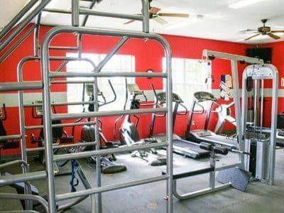 A gym room features red walls, grey flooring, and various exercise equipment including treadmills — 529 SW 39th Cove, Okeechobee FL 34974, OKEECHOBEE, FL