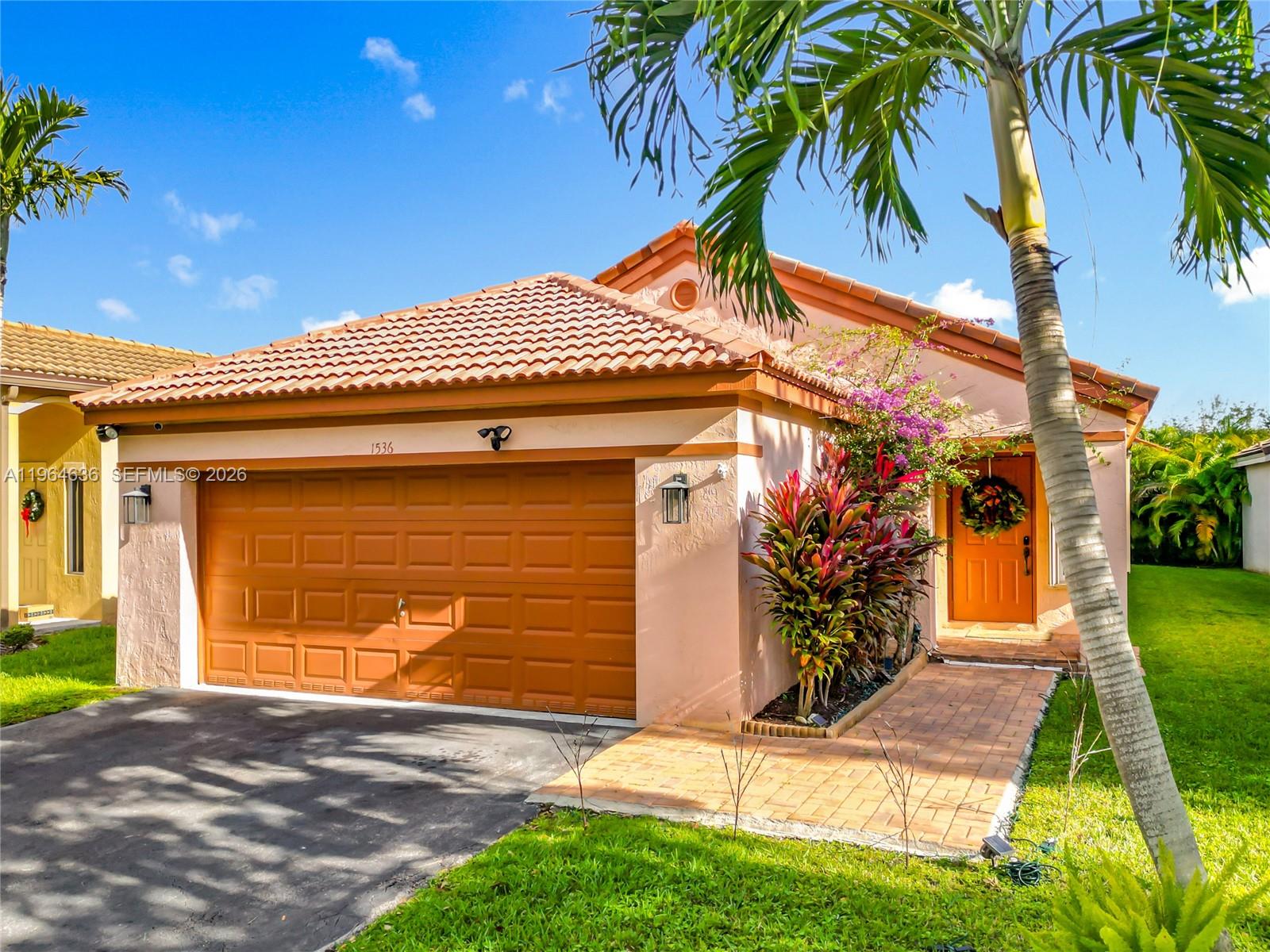 A single-story house with a tan stucco exterior, orange garage door, and a tiled roof — 1536 Presidio Dr, Weston FL 33327, WESTON, FL