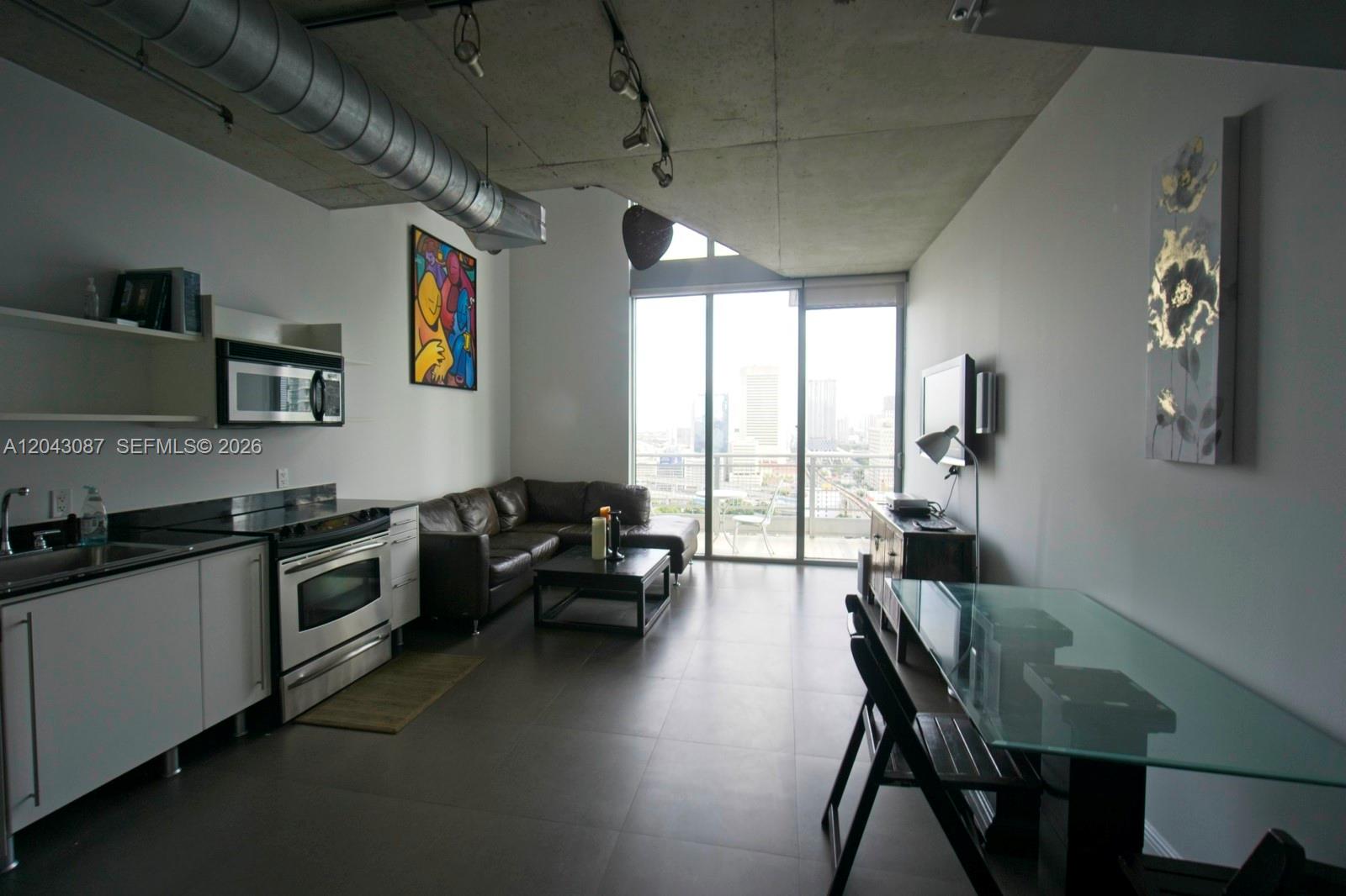 A modern open-concept living area features a kitchen, leather sofa, and industrial-style metal staircase — 690 SW 1 Ct # 2703, Miami FL 33130, MIAMI, FL