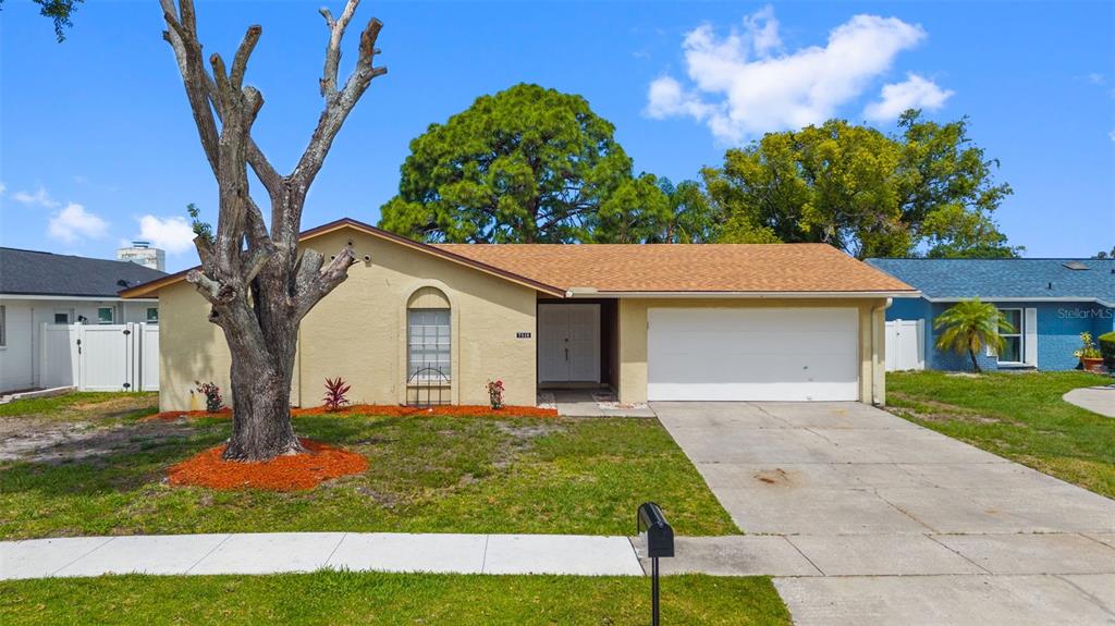 A single-story house with a tan stucco exterior, a two-car garage, and a large tree — 7516 ARMAND CIRCLE, TAMPA, FL