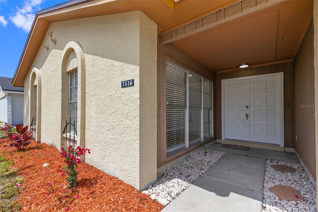 A beige stucco house exterior features a double front door and a landscaped walkway — 7516 ARMAND CIRCLE, TAMPA, FL