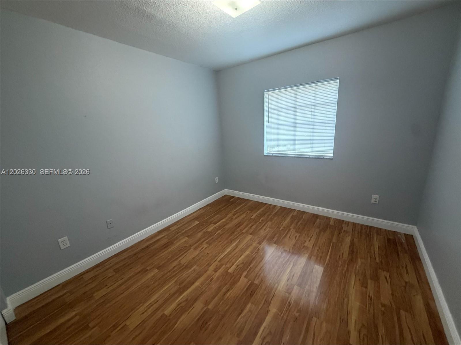 An empty bedroom features light gray walls, wood-look flooring, and a single window with blinds — 14773 SW 9th Ln # 0, Miami FL 33194, MIAMI, FL