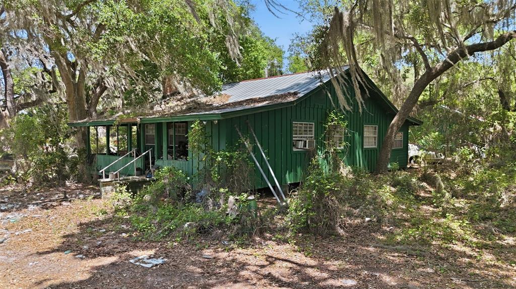 A green, weathered wooden house sits among trees with a metal roof and front porch — 16050 SE 275TH AVENUE, UMATILLA, FL