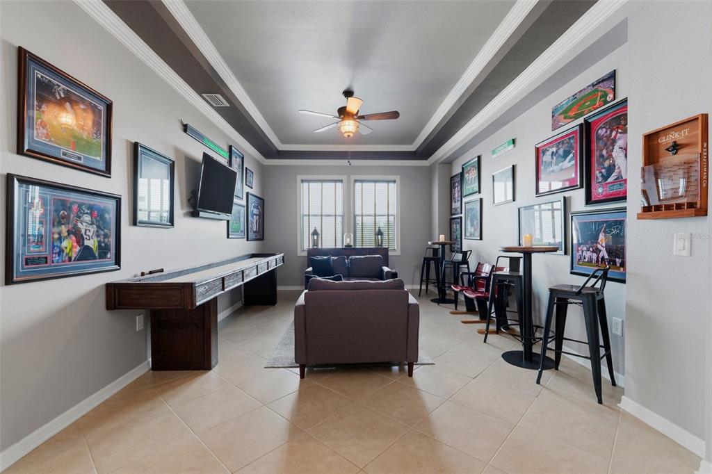 A game room features a shuffleboard table, a sofa, bar seating, and sports memorabilia — 4107 WINDCREST DRIVE, WESLEY CHAPEL, FL
