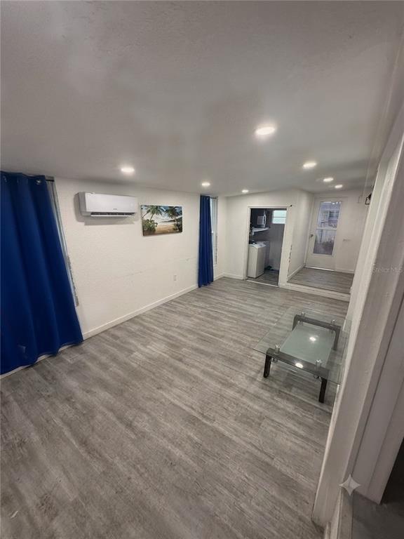 A living room with light wood-look flooring, recessed lighting, a wall-mounted air conditioner, and blue curtains — 2346 DRUID STREET UNIT 1616, CLEARWATER, FL