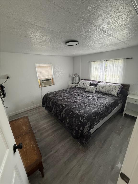 A bedroom with a large bed, light wood-look flooring, and a window air conditioning unit — 2346 DRUID STREET UNIT 1616, CLEARWATER, FL