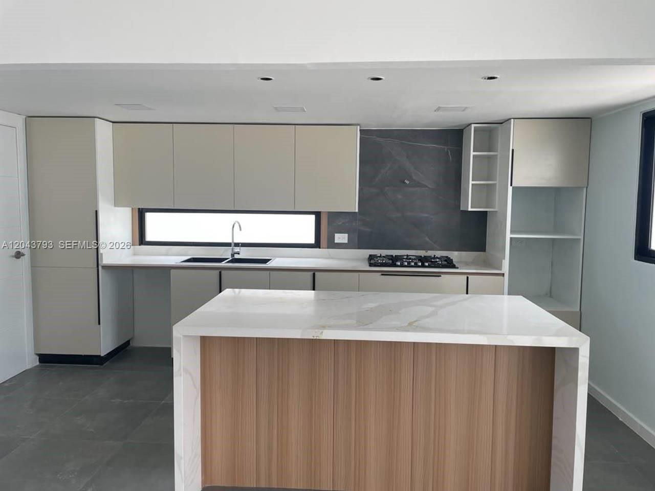 A modern kitchen features light-colored cabinetry, a marble-topped island, and a dark stone backsplash — 0 residencial brisas, FL