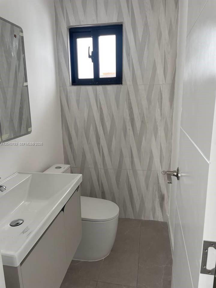 A small bathroom features a white vanity, a toilet, and gray patterned wall tiles — 0 residencial brisas, FL