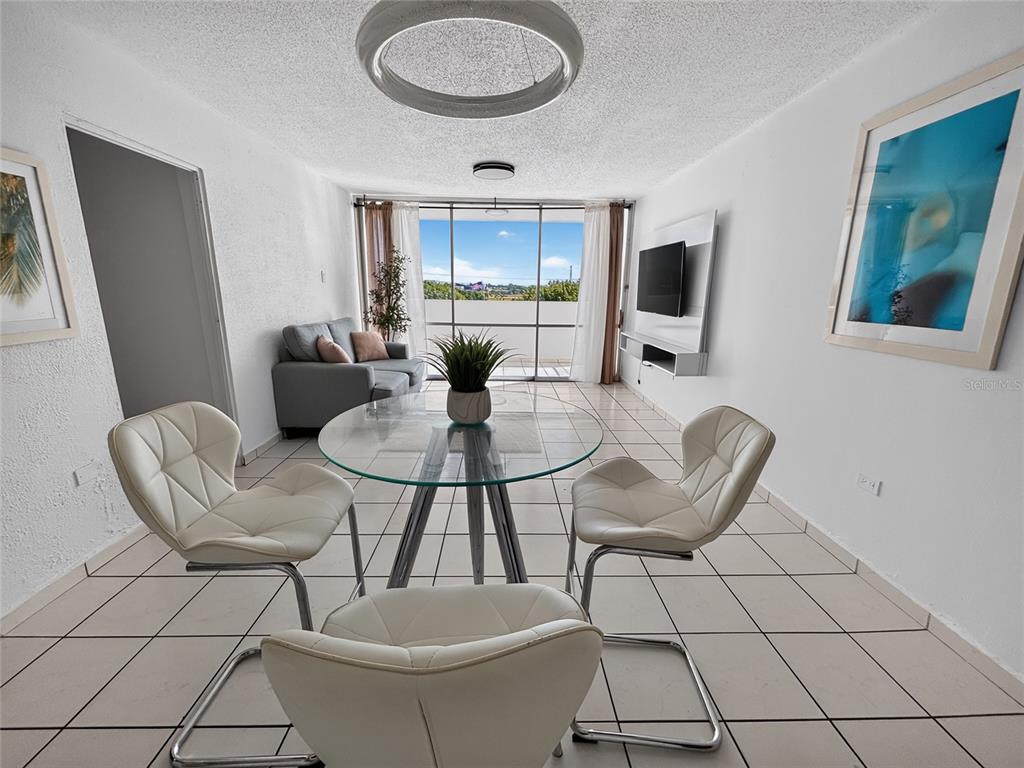 A dining area with a glass table and white chairs sits before a balcony view — K CONDOMINIO INTERSUITES APT 5, CAROLINA, PR