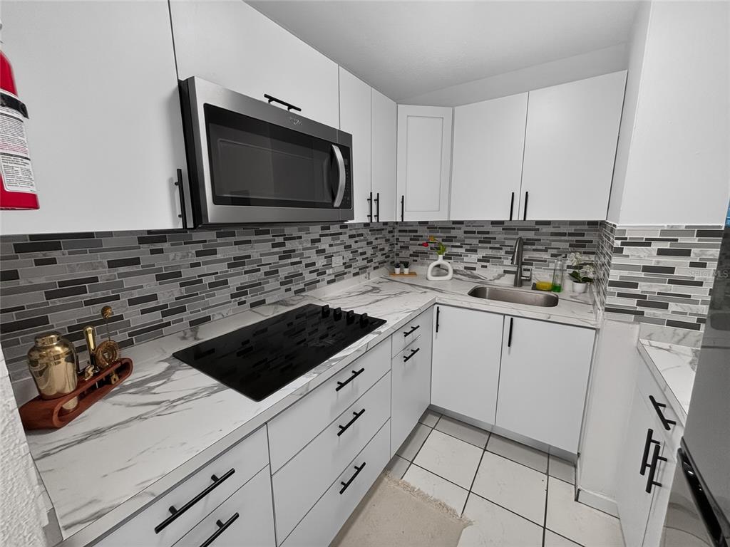 A kitchen features white cabinets, a black cooktop, a stainless steel microwave, and marble-patterned countertops — K CONDOMINIO INTERSUITES APT 5, CAROLINA, PR