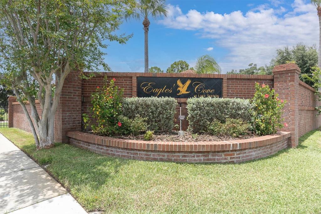 A brick entrance sign for Eagles' Cove at Lake Tarpon sits behind a landscaped garden — 4270 COVE DRIVE, PALM HARBOR, FL