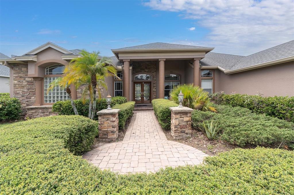 A stone-paved walkway leads to the front entrance of a house with stone accents — 4270 COVE DRIVE, PALM HARBOR, FL