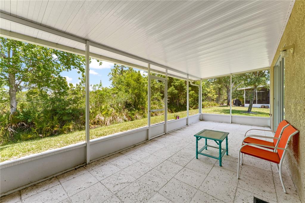 A screened-in patio with white tile flooring, a metal roof, and two orange chairs — 19182 LAKE AUDUBON DRIVE, TAMPA, FL