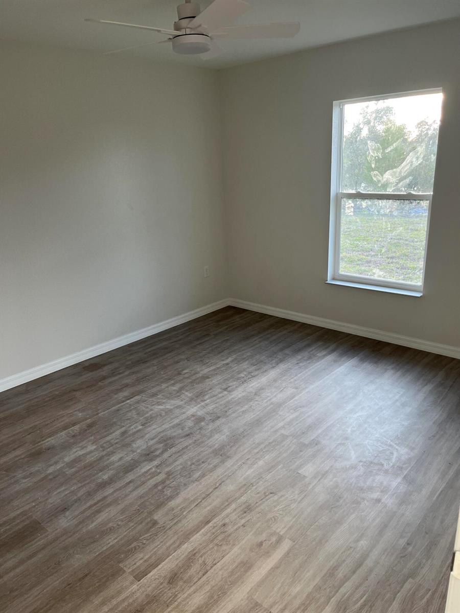 An empty bedroom with light gray walls, wood-look flooring, a ceiling fan, and a window — 7056 San Benito Drive, Sebring FL 33872, SEBRING, FL
