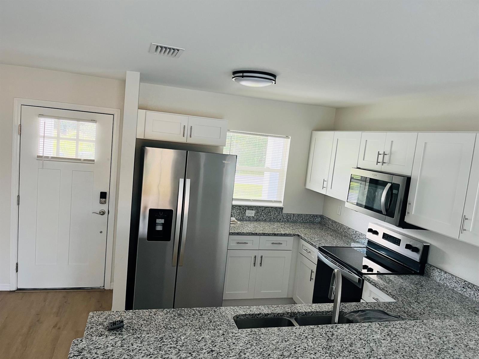 A kitchen features white cabinets, granite countertops, stainless steel appliances, and a double sink — 7056 San Benito Drive, Sebring FL 33872, SEBRING, FL