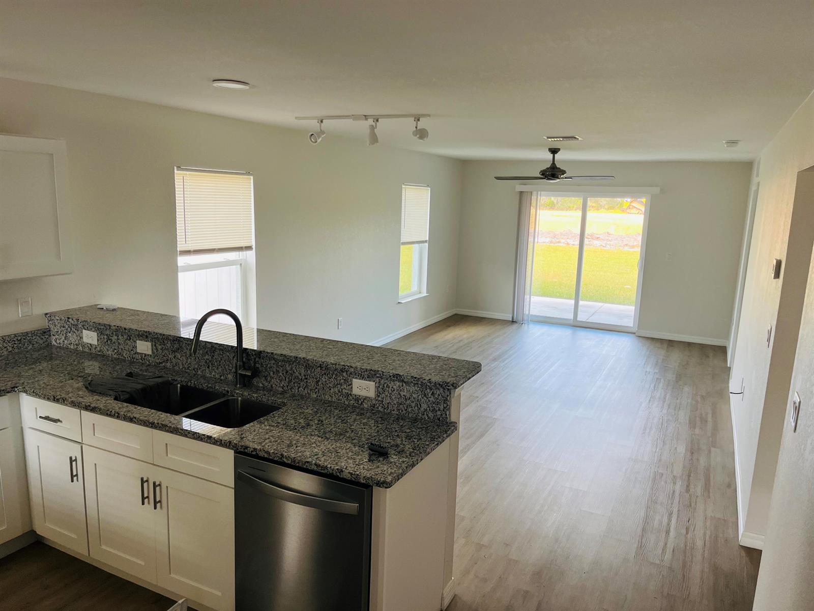 A kitchen with granite countertops and white cabinets overlooks an open living area with flooring — 7056 San Benito Drive, Sebring FL 33872, SEBRING, FL