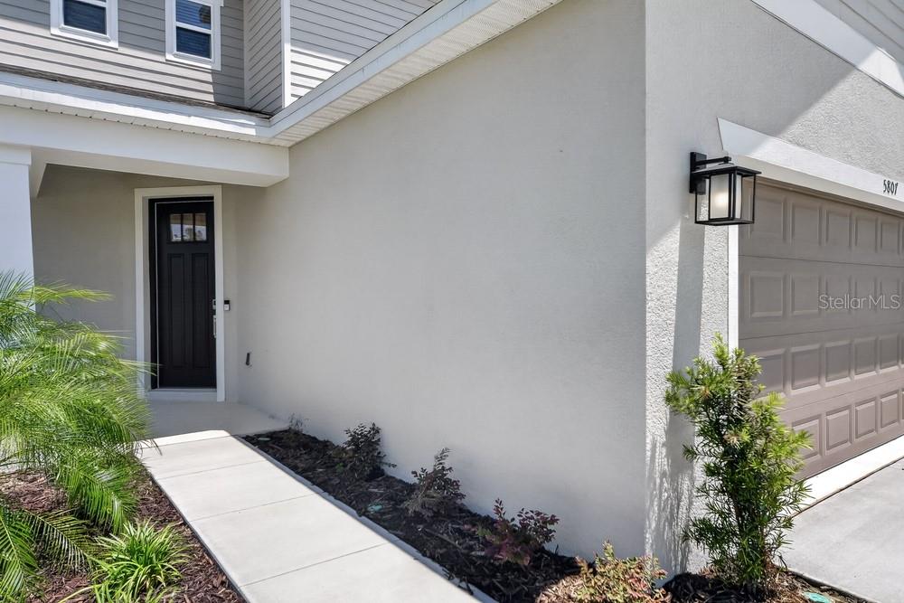 A concrete walkway leads to the dark front door of a house with a garage — 5807 PORTICO PLACE, KISSIMMEE, FL