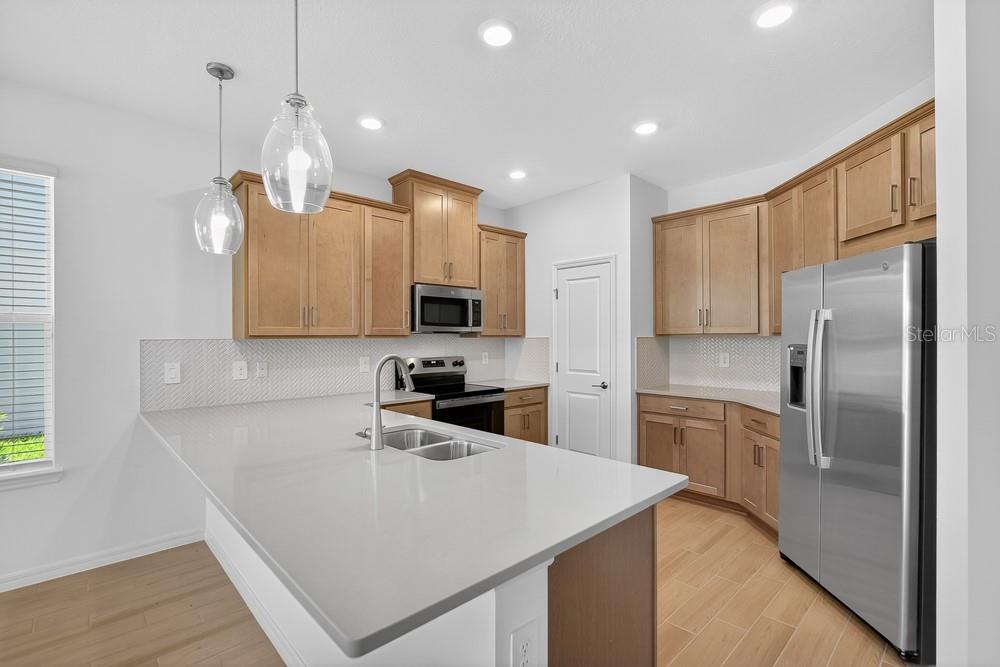 A kitchen features light wood cabinets, a gray quartz countertop, and stainless steel appliances — 5807 PORTICO PLACE, KISSIMMEE, FL