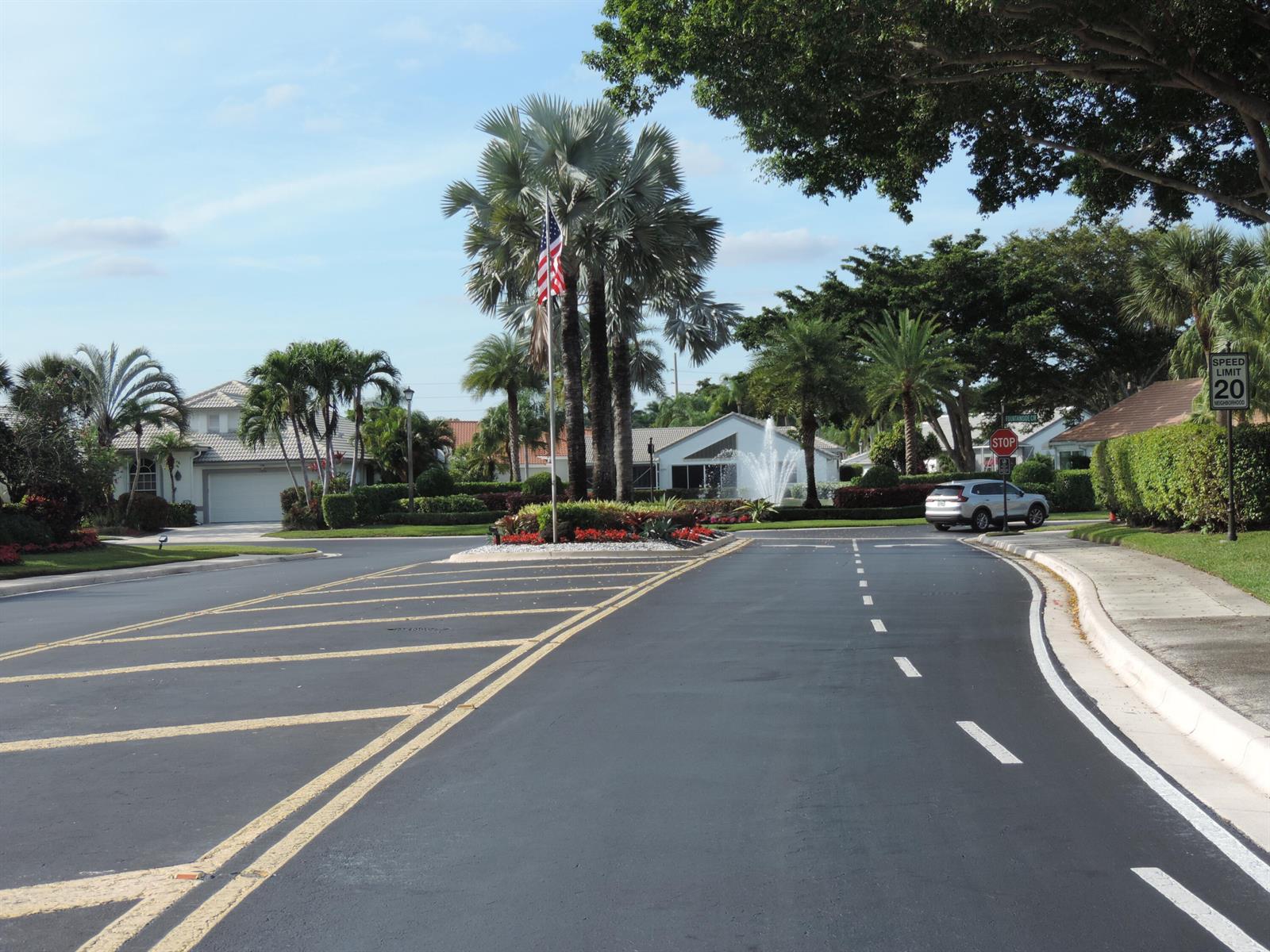A residential street features a landscaped traffic island with a fountain and an American flag — 6375 Three Lakes Lane, Boynton Beach FL 33437, BOYNTON BEACH, FL