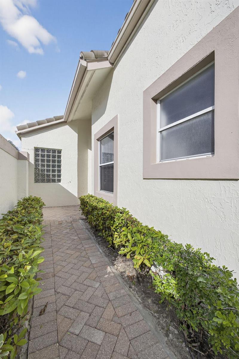 A brick walkway leads along the side of a stucco house with two windows — 6375 Three Lakes Lane, Boynton Beach FL 33437, BOYNTON BEACH, FL