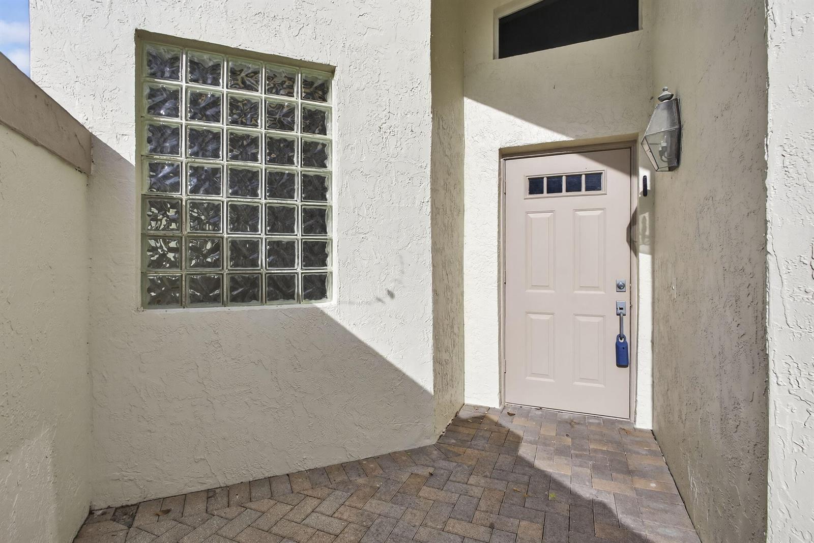A beige front door and a glass block window are set in a stucco wall — 6375 Three Lakes Lane, Boynton Beach FL 33437, BOYNTON BEACH, FL