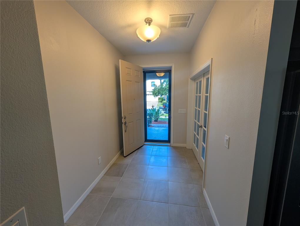 An entryway features light-colored tile flooring, a beige front door, and a glass-paneled door — 2358 KENNINGTON COVE, DELAND, FL