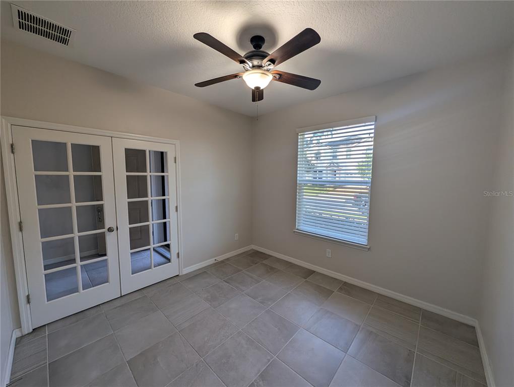 A room with light gray walls, tile flooring, a ceiling fan, and white French doors — 2358 KENNINGTON COVE, DELAND, FL
