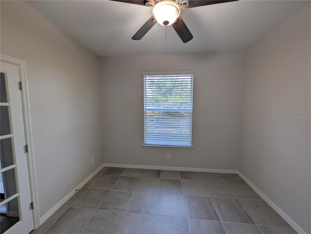 An empty room features light-colored walls, a ceiling fan, a window with blinds, and tiled flooring — 2358 KENNINGTON COVE, DELAND, FL
