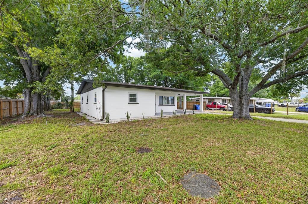 A white, single-story house with a covered porch sits on a grassy lot with trees — 204 7TH AVENUE NW, RUSKIN, FL