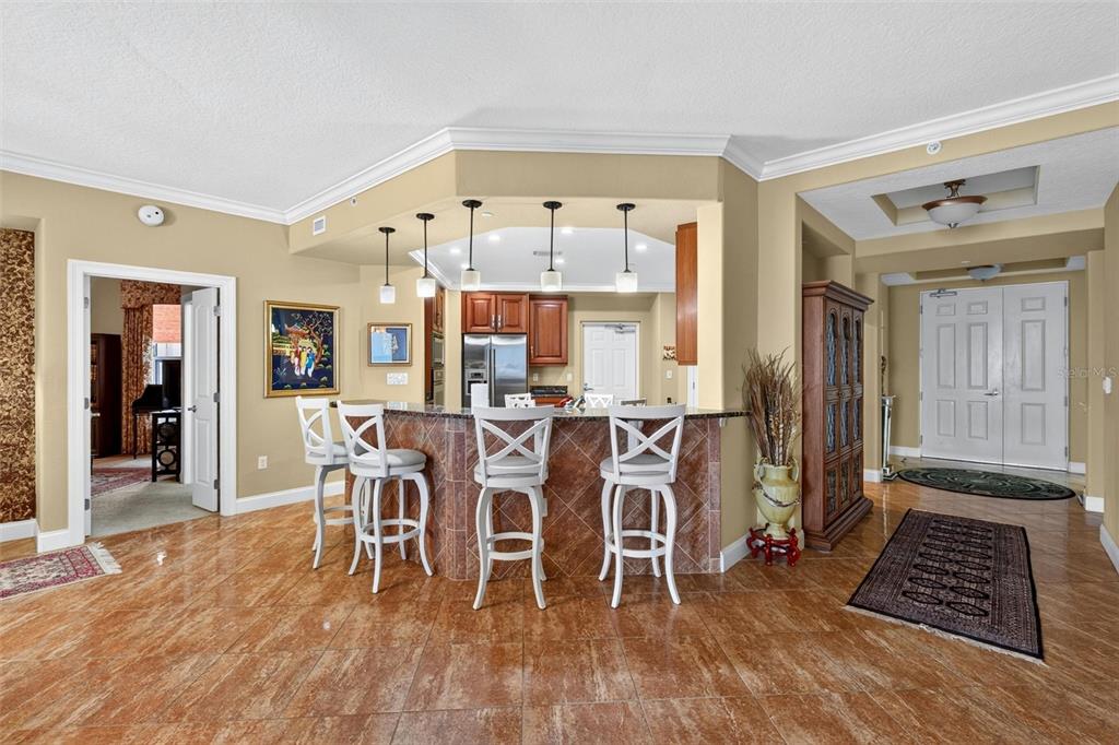 A kitchen with a breakfast bar, stools, and tile flooring opens into a living area — 3245 S ATLANTIC AVENUE UNIT 1002, DAYTONA BEACH SHORES, FL