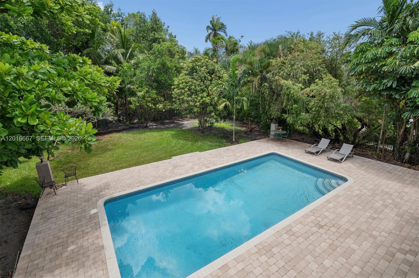 A rectangular swimming pool sits on a paved patio next to a grassy backyard — 20021 NE 25th Ave, Miami FL 33180, MIAMI, FL