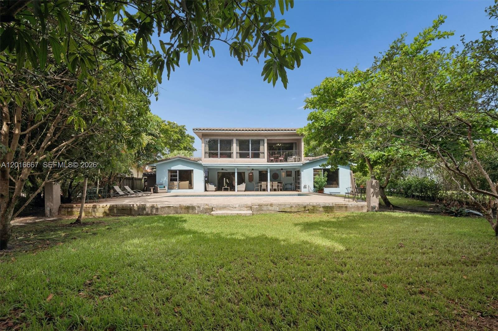 A two-story house with a backyard pool, patio, and surrounding trees under a clear sky — 20021 NE 25th Ave, Miami FL 33180, MIAMI, FL