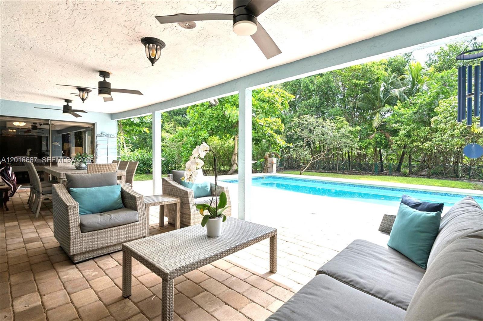 A covered patio features wicker furniture, a coffee table, and a view of a pool — 20021 NE 25th Ave, Miami FL 33180, MIAMI, FL