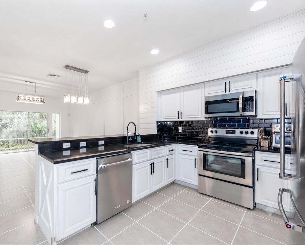A modern kitchen features white cabinets, black countertops, a subway tile backsplash, and stainless appliances — 4466 Leo Lane, Riviera Beach FL 33410, RIVIERA BEACH, FL