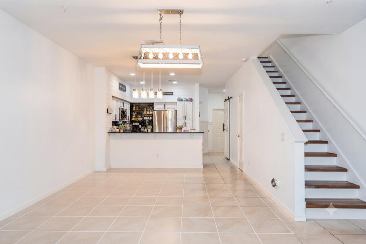 An open-concept room features tile flooring, a kitchen breakfast bar, and a wooden staircase — 4466 Leo Lane, Riviera Beach FL 33410, RIVIERA BEACH, FL
